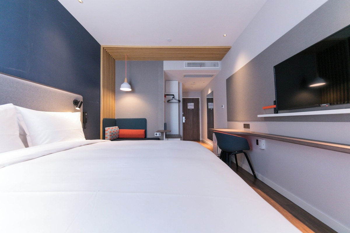 Ett modernt hotellrum med en stor säng, ett skrivbord, en tv och en sittgrupp med en stol och ett litet bord.