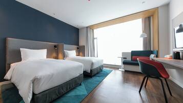 A hotel room with two beds, a desk, a chair, and a large window.