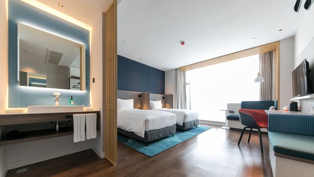A modern hotel room with a large bed, a desk, a chair, a TV, and a bathroom with a mirror and sink. - Holiday Inn Express Shanghai Tangzhen by IHG (Shanghai)