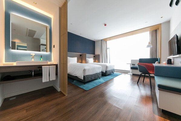 Ein modernes Hotelzimmer mit einem großen Bett, einem Schreibtisch, einem Stuhl, einem Fernseher und einem Badezimmer mit Spiegel und Waschbecken.