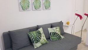 A grey sofa with two green and white patterned pillows, a white wall with four framed leaf artworks, and a small white shelf with a yellow object. - Casa Viviana - Bari Policlinico (Bari)