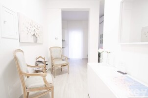 Una stanza luminosa e bianca con due sedie di legno, un tavolo bianco e un quadro appeso al muro.