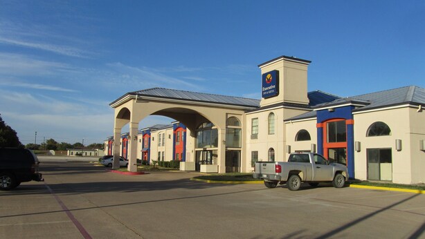 A hotel with a central archway, multiple suites, and a parking lot. - Executive Inn and suites, independent hotel (Wichita Falls)