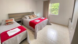 Una habitación de hotel con dos camas, un ventanal grande con cortinas y suelo de baldosas.