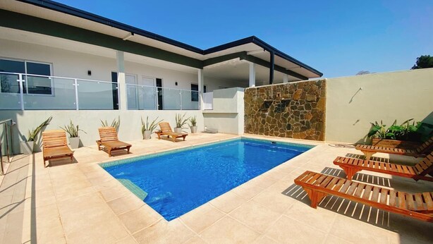 Un área de piscina moderna con una piscina rectangular, tumbonas de madera y un muro de piedra.