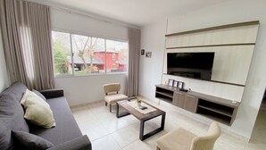 Una sala de estar moderna con un sofá, dos sillones, una mesa de centro y un televisor montado en la pared.