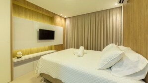 A hotel room with a bed, a flat-screen TV mounted on the wall, and a bedside table with a lamp. - Hotel Home Vacations (Natal)