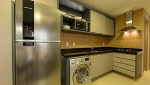 A modern kitchen with stainless steel appliances, including a refrigerator, microwave, and washing machine, with wooden cabinetry and a gas stove. - Hotel Home Vacations (Natal)