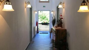 A hallway with tiled flooring, wall-mounted lights, a wooden ceiling, and a view of the outdoors through a window. - Hotel Garni Zum Holzfäller (Wernigerode)