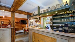 A rustic bar area with wooden beams, shelves of glassware, and a wooden counter with a village scene engraving. - Hotel Garni Zum Holzfäller (Wernigerode)