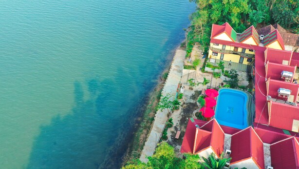 An aerial view of a coastal hotel with multiple red-roofed buildings, a swimming pool, and a clear view of the adjacent turquoise sea. - Phong Nha Escape Bungalow (Phong Nha)