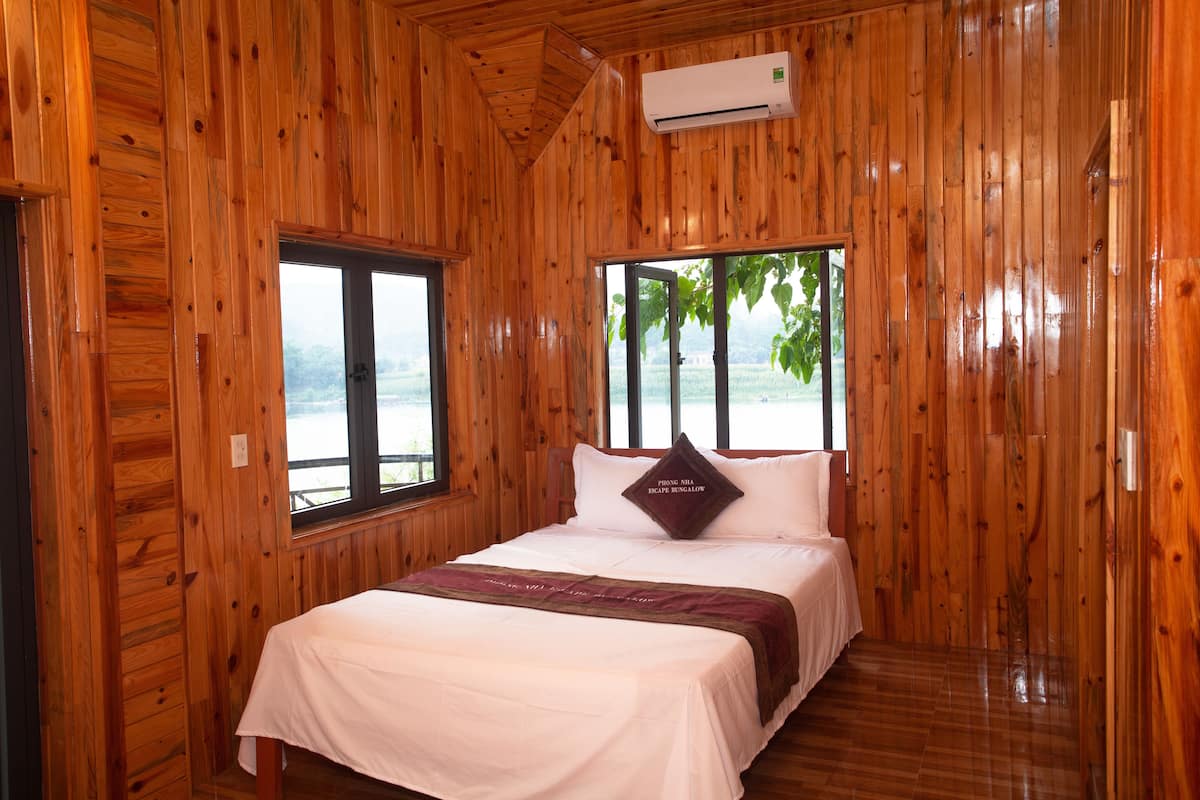 A wooden-paneled room with a bed, a window, and an air conditioning unit.