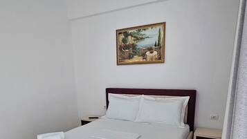 Ein ordentlich bezogenes Bett mit weißen Leinen und Handtüchern, ein Landschaftsbild an der Wand und ein Nachttisch mit Lampe.
