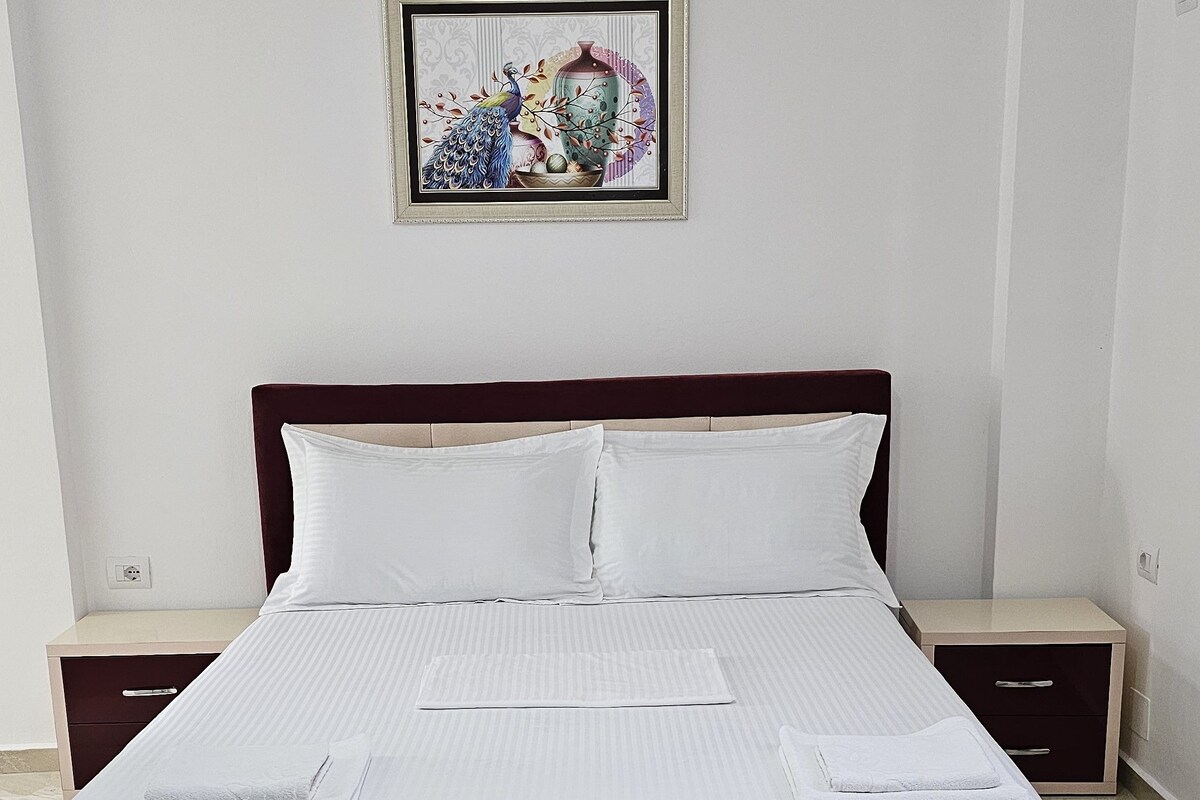Ein ordentlich bezogenes Bett mit weißen Leinen und Kissen, ein hölzerner Kopfteil und ein gerahmtes Bild an der Wand.