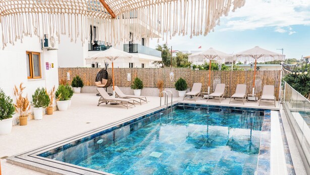 Una piscina con sillas de descanso, una zona de estar cubierta y plantas en macetas.