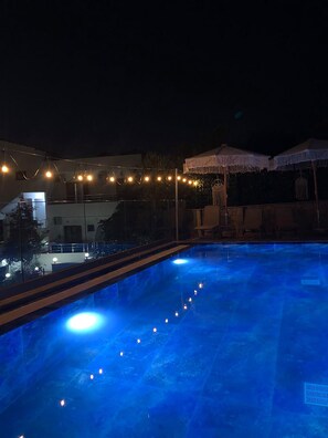 An outdoor swimming pool at night with string lights and white umbrellas. - Vila Finnley (Ksamil)