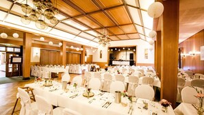Un salón de banquetes con mesas redondas dispuestas para un evento formal, con manteles blancos, sillas y centros de mesa florales.