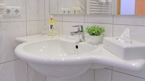 A white bathroom sink with a modern faucet, a small potted plant, and a tissue box. - Triple room - Landhotel Zur Eiche (Buxtehude)
