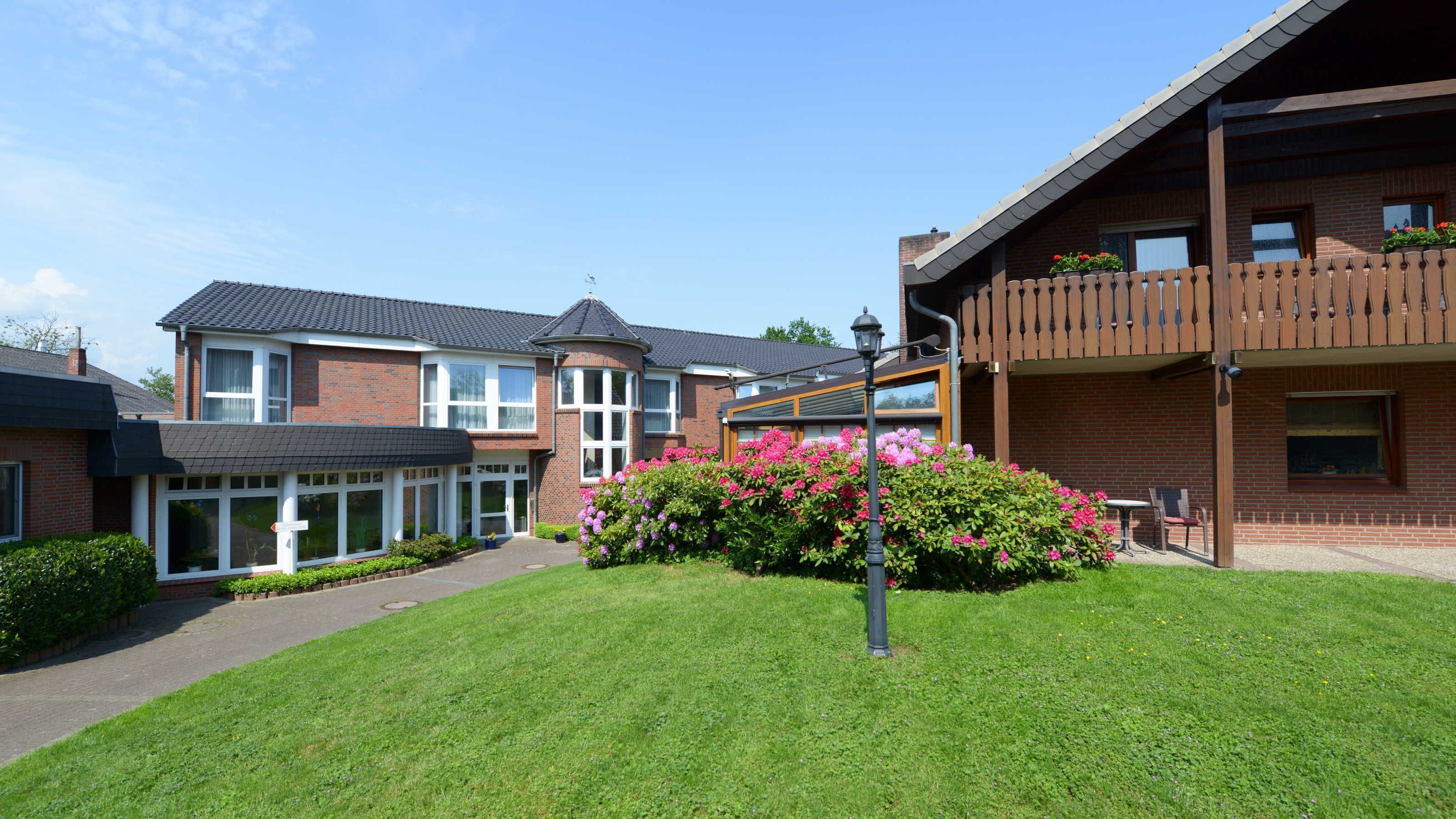 A residential building with a brick facade, large windows, and a well-maintained lawn with flowering bushes.