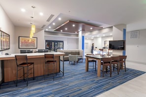 A modern kitchen with a bar area, seating, and a large TV. - Holiday Inn Express & Suites Columbus - Worthington by IHG (Columbus)