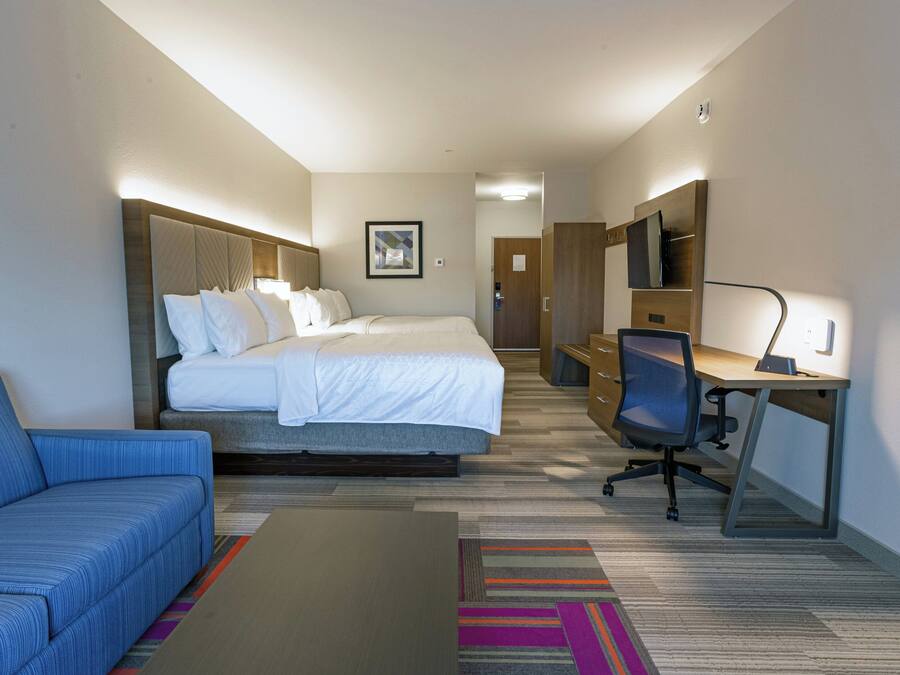 A hotel room with a bed, a desk, a chair, a sofa, and a TV.