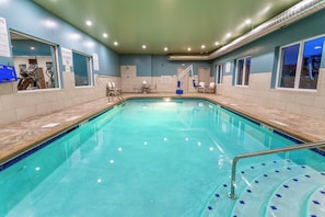 An indoor swimming pool with a tiled edge, a pool ladder, and a seating area with chairs and a table. - Holiday Inn Express & Suites Columbus - Worthington by IHG (Columbus)