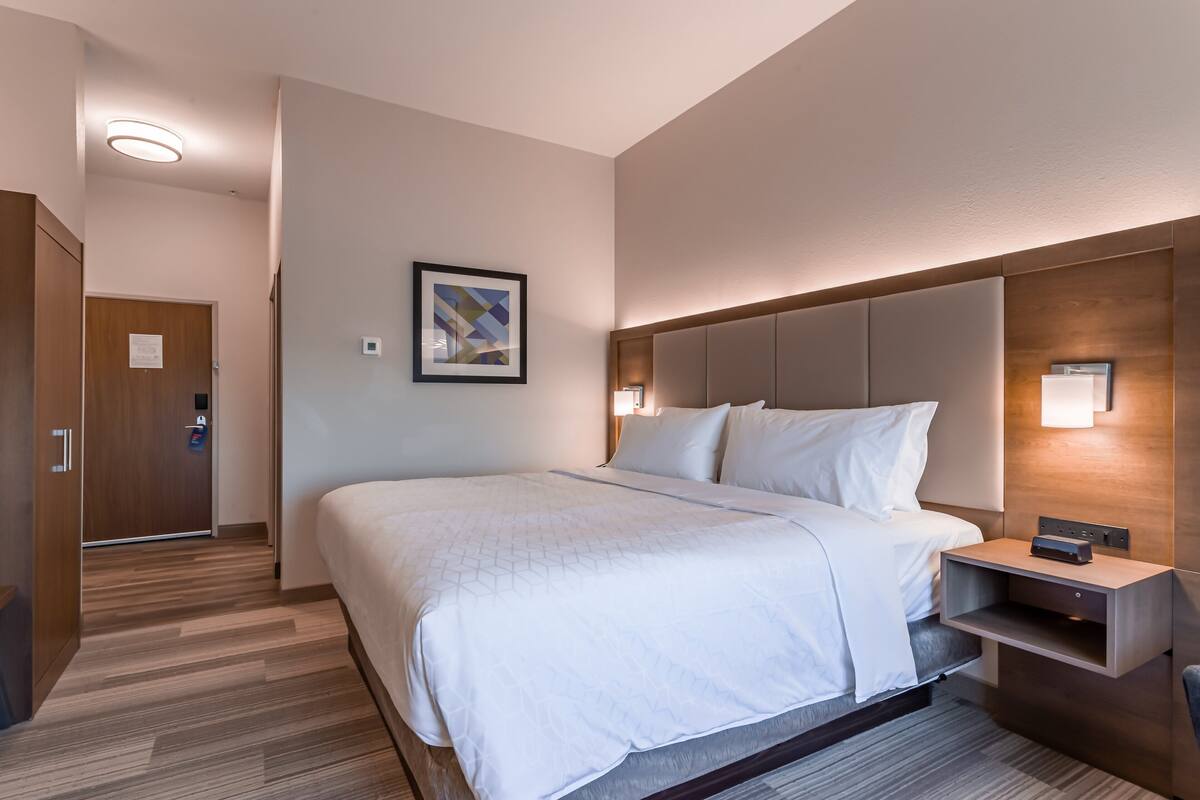 A hotel room with a large bed, a bedside table, a wall-mounted light, and a door with a lock.
