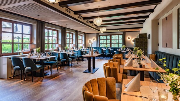 A spacious restaurant with multiple dining areas, large windows, and modern lighting fixtures.