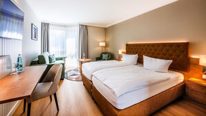 A hotel room with two beds, a desk, a chair, a small table, and a sofa.