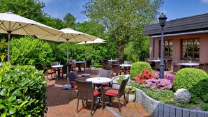 An outdoor patio area with brick flooring, wicker furniture, and large umbrellas providing shade.