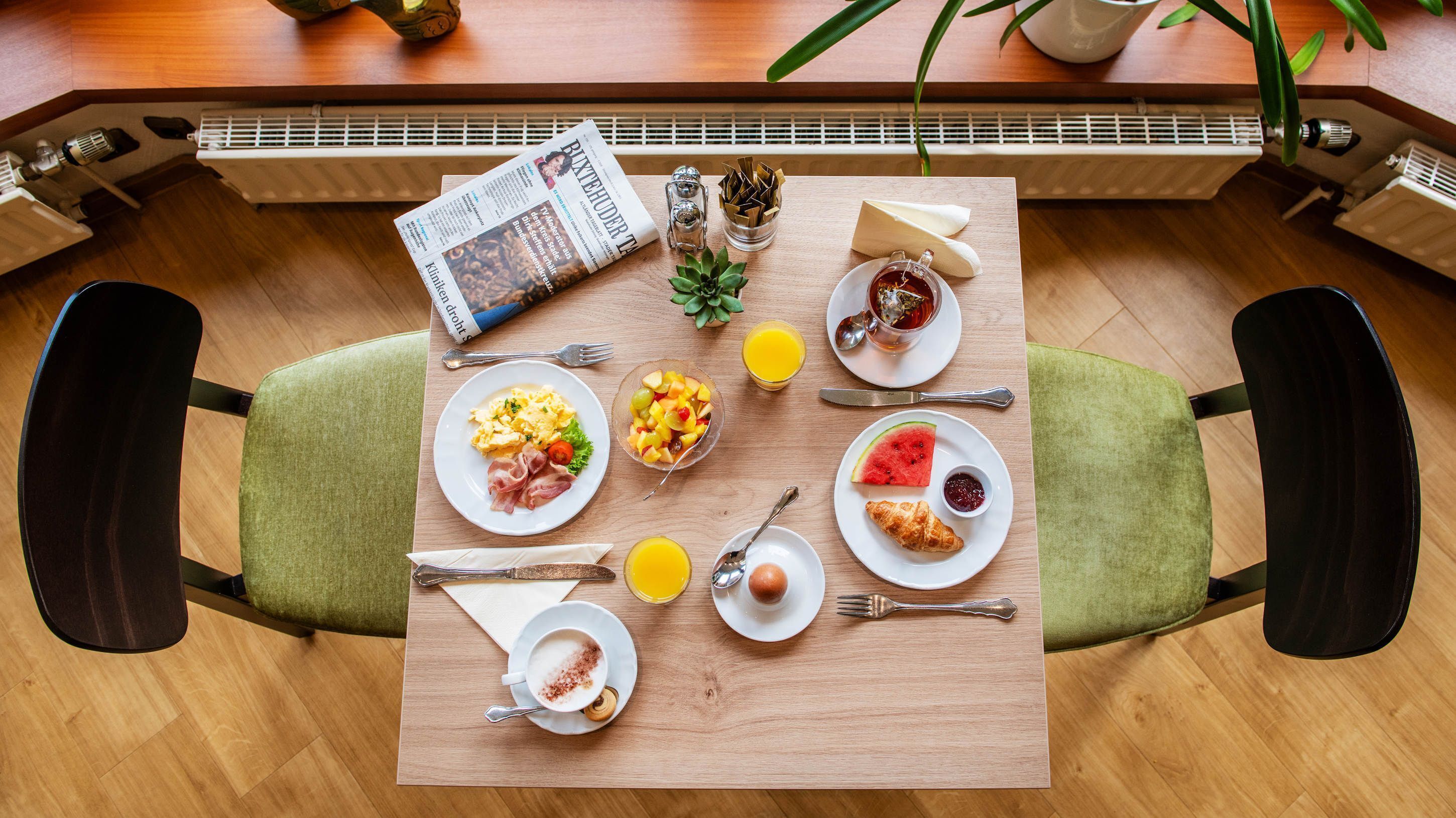A breakfast table with plates of food, drinks, and a newspaper.