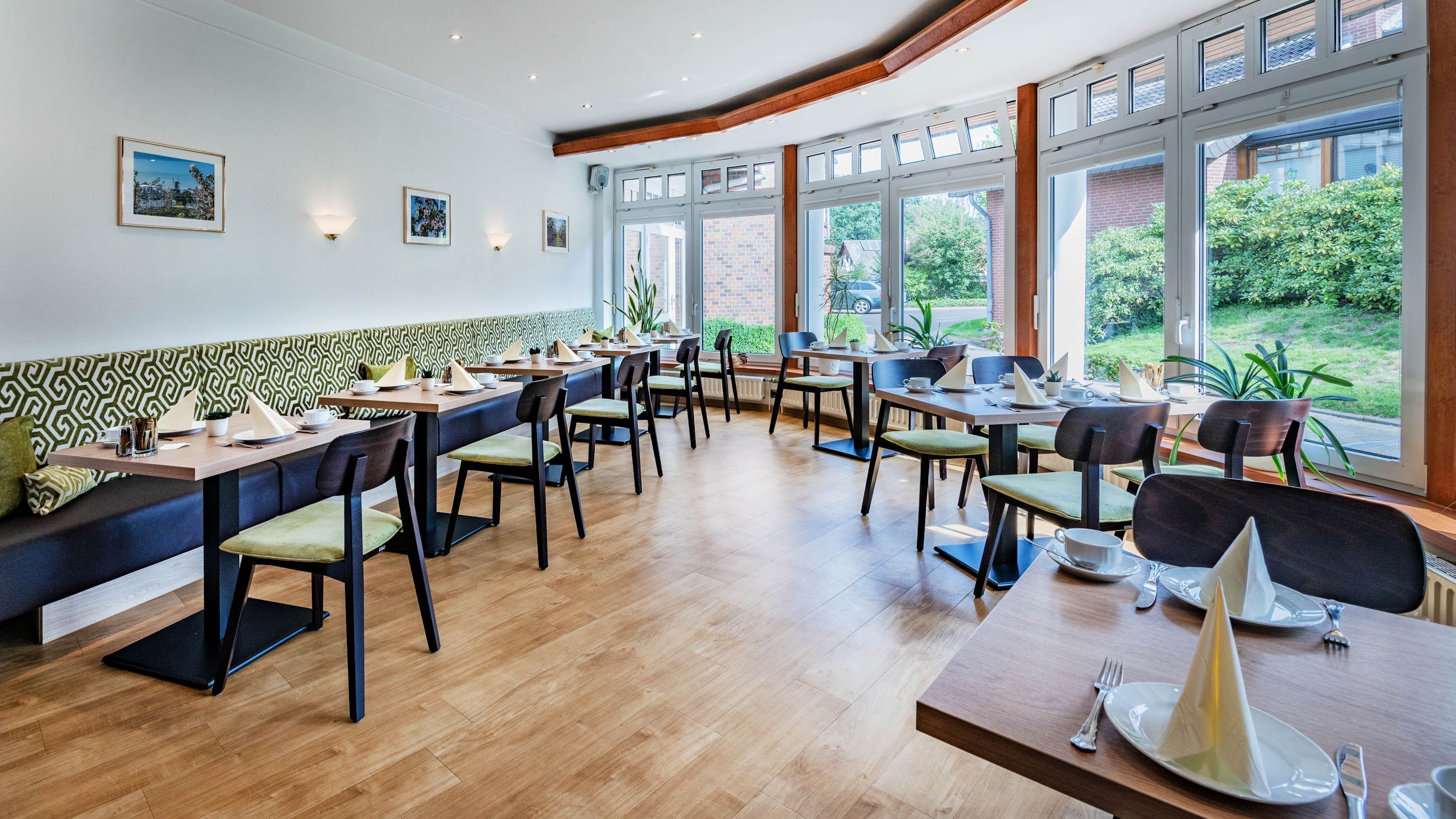 Un restaurante con suelo de madera, asientos de diseño verde y ventanas amplias que dan a zonas verdes.