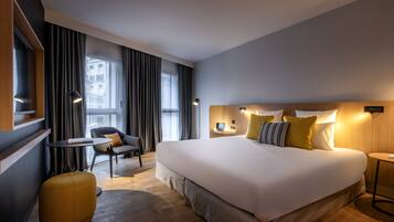Een moderne hotelkamer met een groot bed, een kleine ronde tafel, een bank en een geel poef.