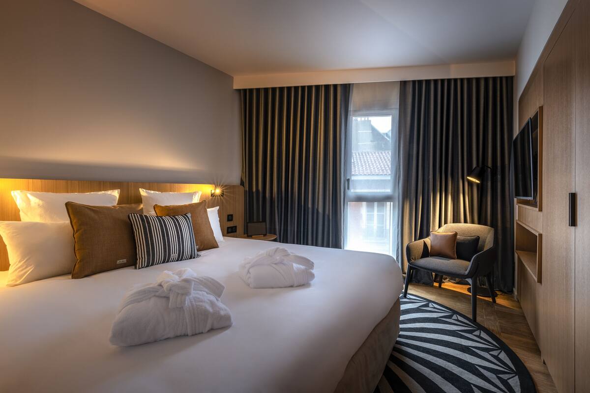 Une chambre d’hôtel avec un grand lit, une chaise, une télévision et une fenêtre avec des rideaux.