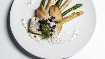 A white plate with a piece of grilled fish, asparagus, and a garnish of purple leaves.