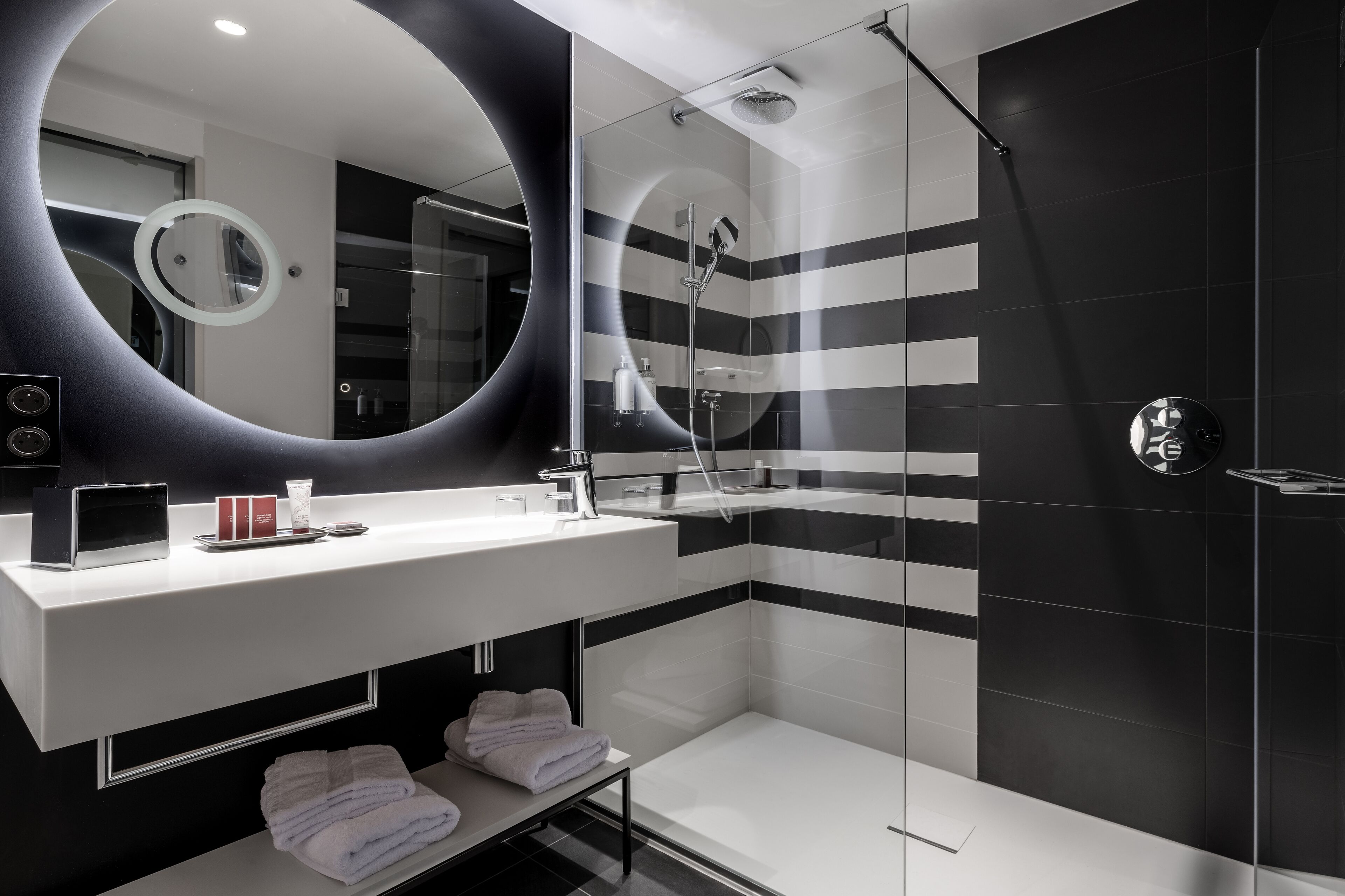 Un baño moderno con un espejo grande, ducha y tocador con artículos de aseo.