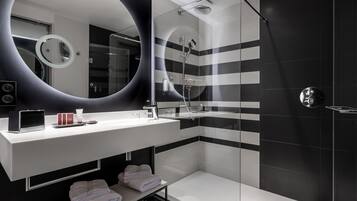 Un baño moderno con un espejo grande, ducha y tocador con artículos de aseo.