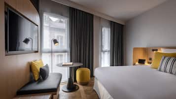 A modern hotel room with a large bed, a small table, a bench, and a sofa.