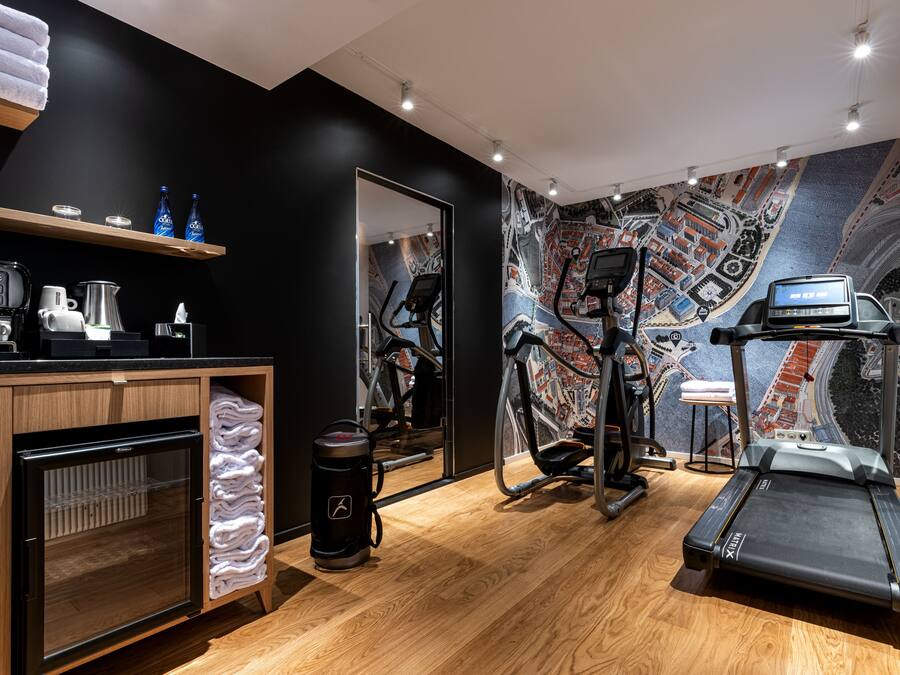 Una habitación de hotel moderna con suelo de madera, una cinta de correr, una bicicleta estática y una máquina de café.