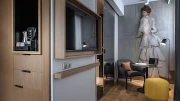 Une chambre moderne avec un meuble en bois, un téléviseur à écran plat, une petite table avec un ordinateur portable et un pouf jaune.