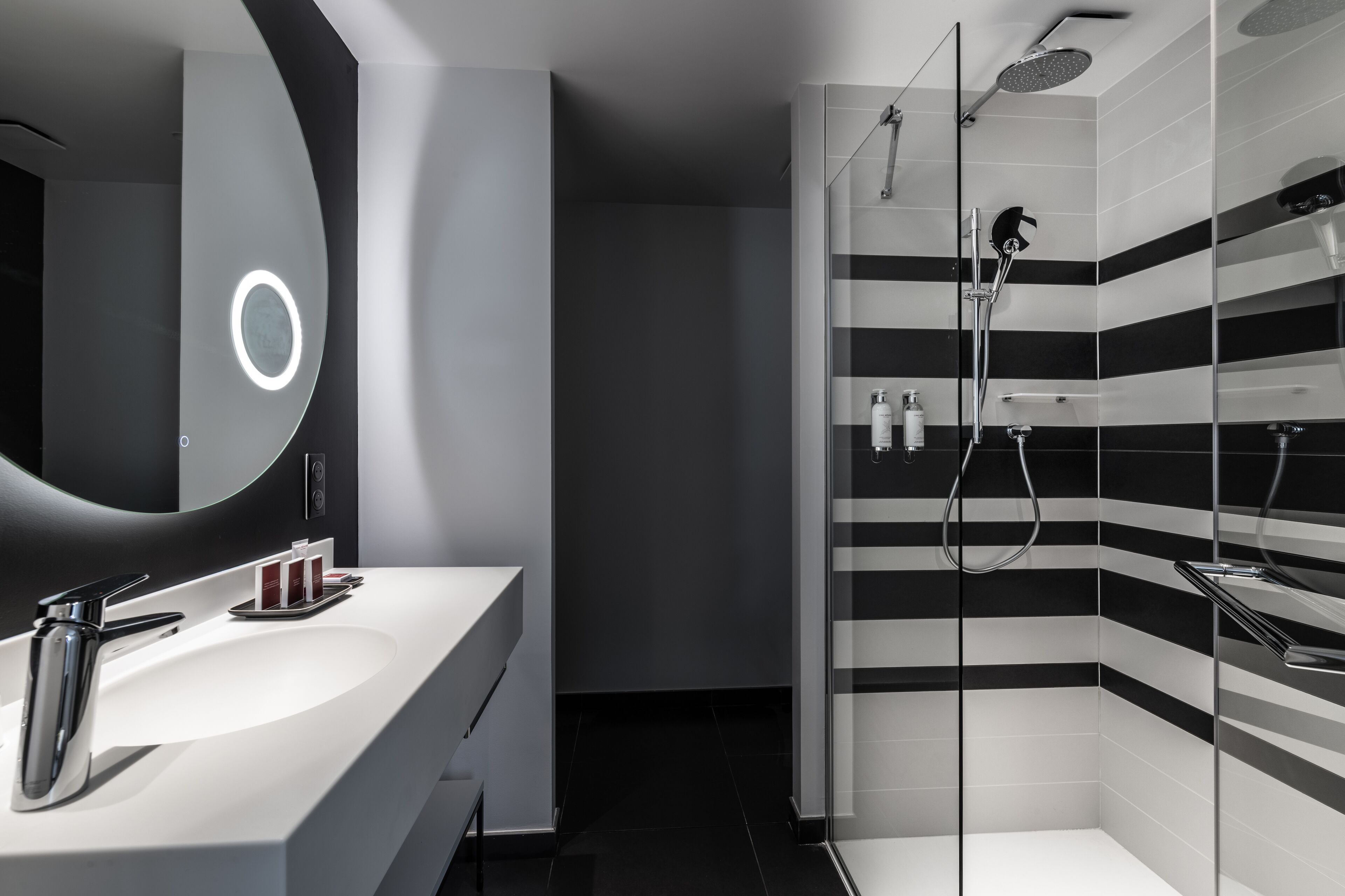 A modern bathroom with a white sink, a large mirror, and a shower with black and white striped tiles.