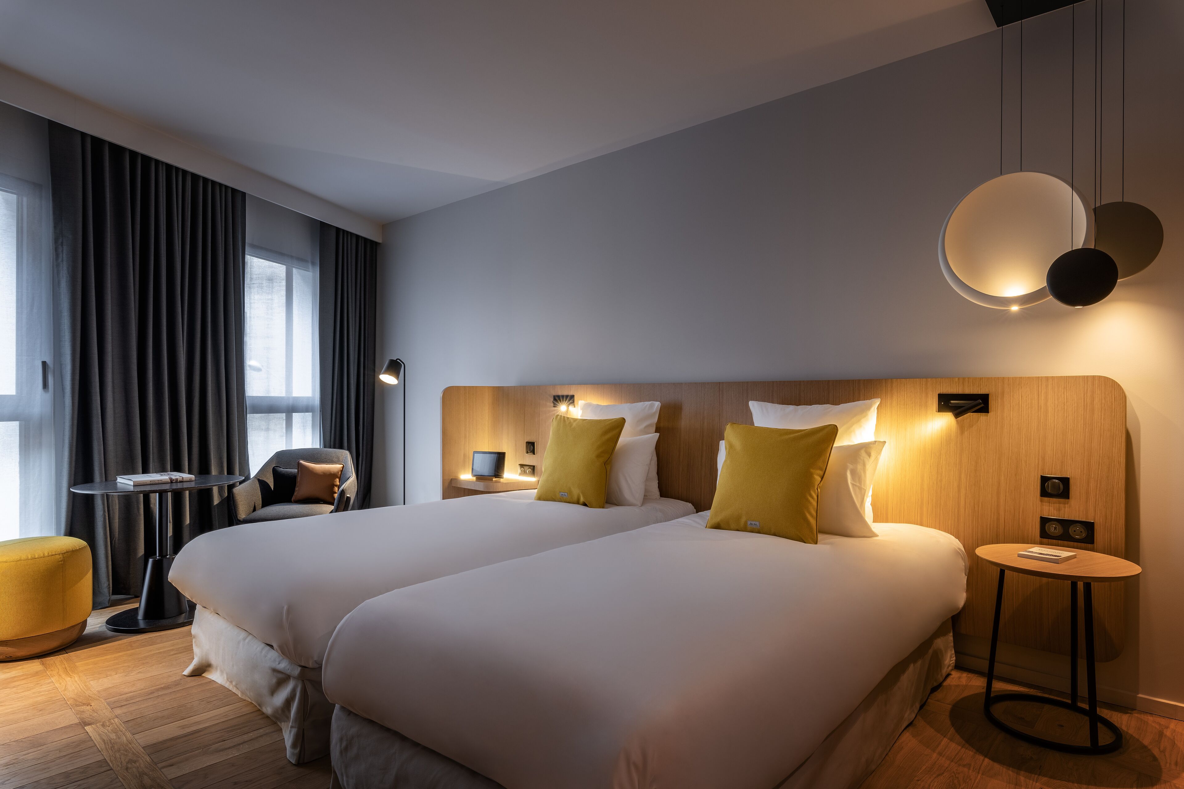 Une chambre d’hôtel avec deux lits, une petite table ronde, un canapé et une grande fenêtre avec des rideaux.