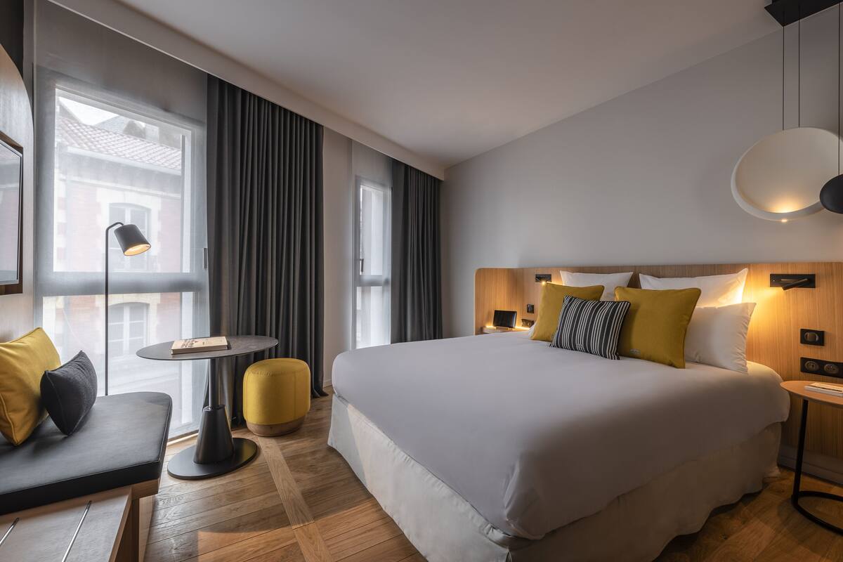Une chambre d’hôtel moderne avec un grand lit, un canapé, une petite table et une lampe.