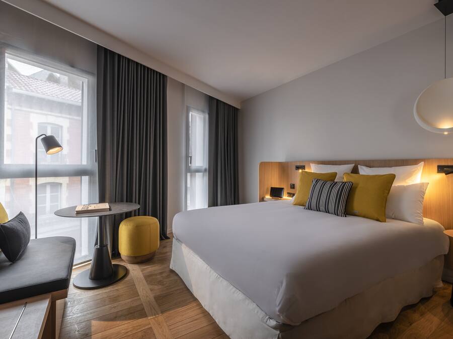 A modern hotel room with a large bed, a sofa, a small table, and a lamp.