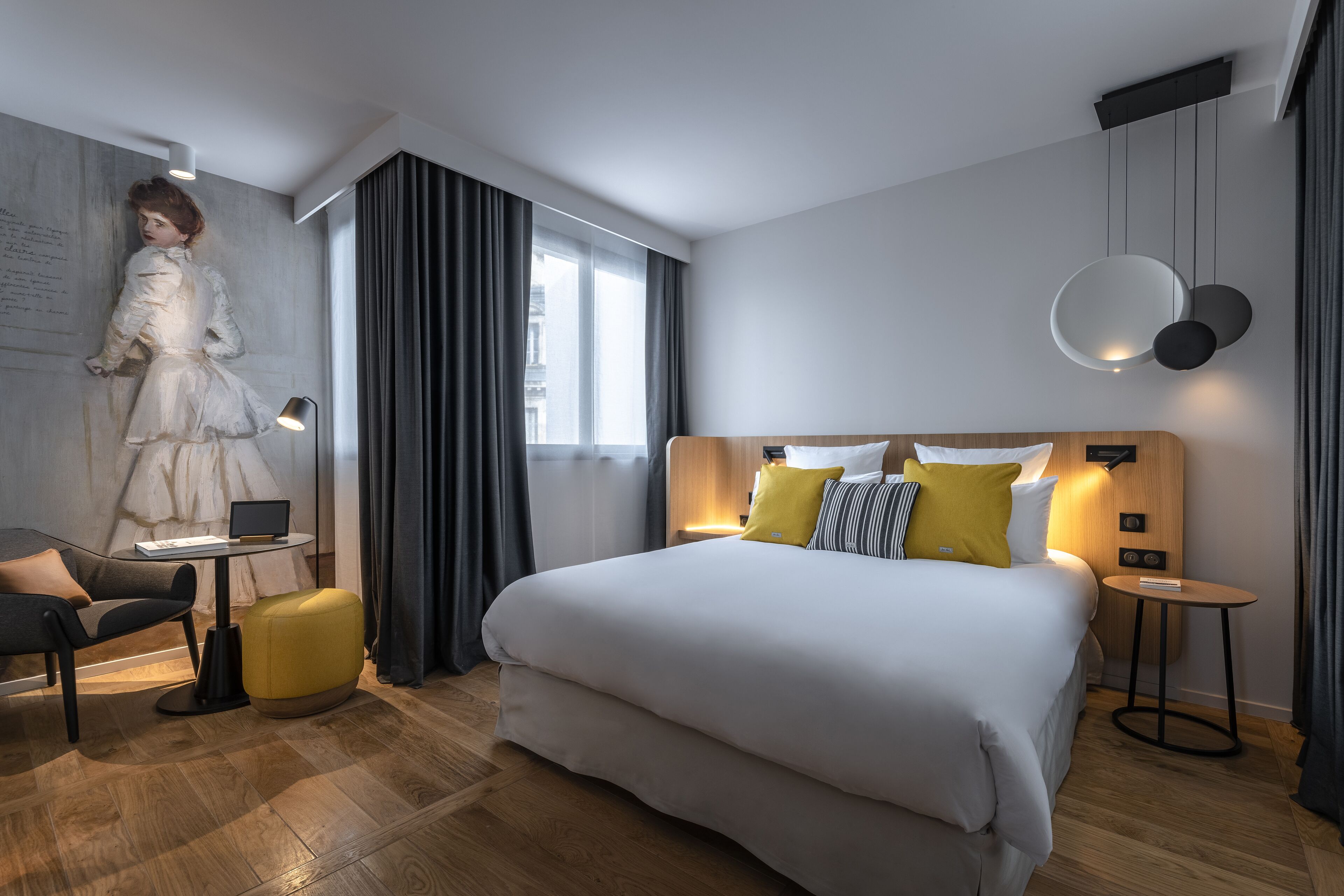 Une chambre d’hôtel moderne avec un grand lit, un bureau, une chaise et une grande fenêtre avec des rideaux.