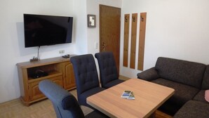 Una sala de estar con un televisor de pantalla plana, un mueble de madera, un sofá y una mesa.