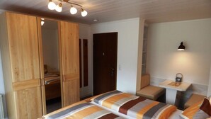 Un dormitorio con dos camas, un armario de madera, un escritorio y una mesita con una lámpara.