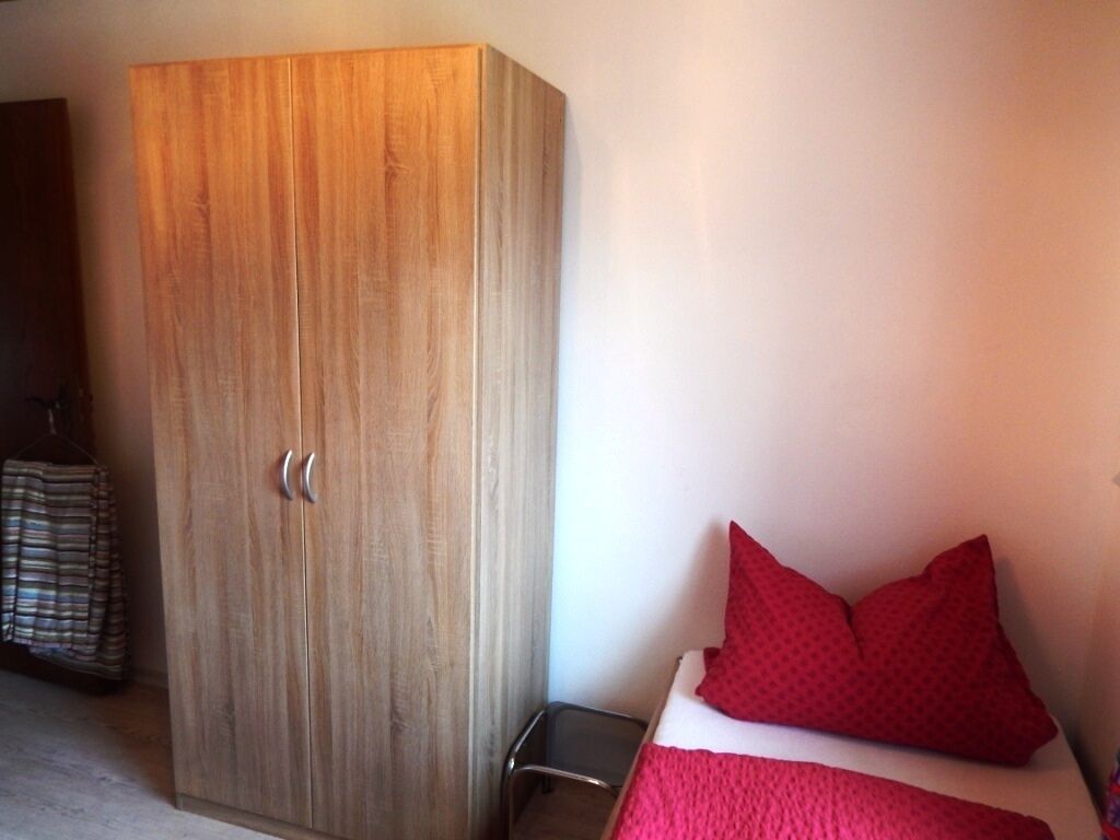 Een slaapkamer met een houten garderobe, een bed met rode beddengoed en een klein nachtkastje.