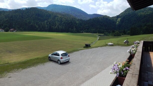 Un coche estacionado en un camino de grava, con vista a un campo verde y montañas al fondo.