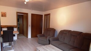 Een woonkamer met een bank, twee fauteuils, een salontafel en een eethoek met een tafel en stoelen.